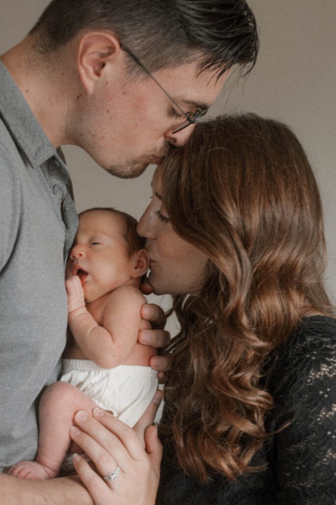 mom kisses baby while dad kisses mom