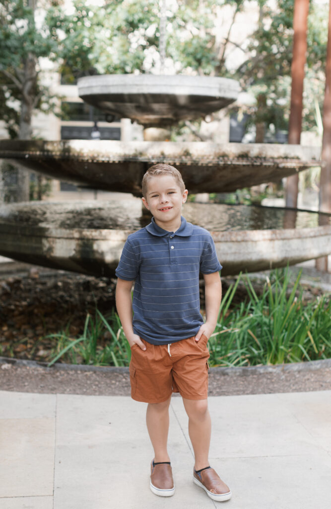 boy stands in front of fountain, hands in pocke