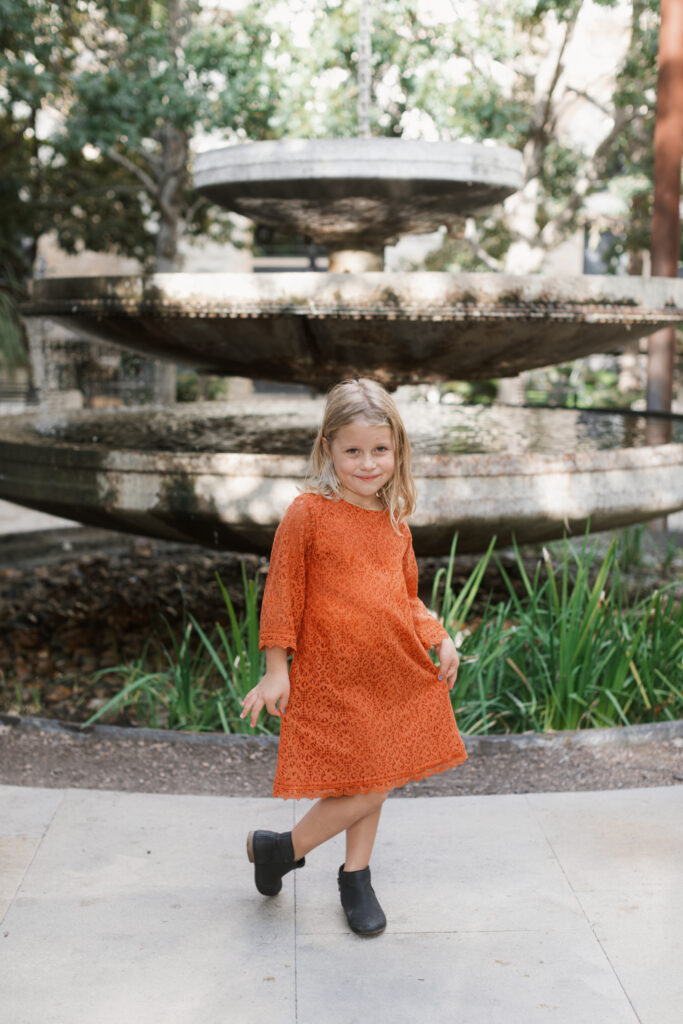 girl stands in front of fountain, doing a curtsey