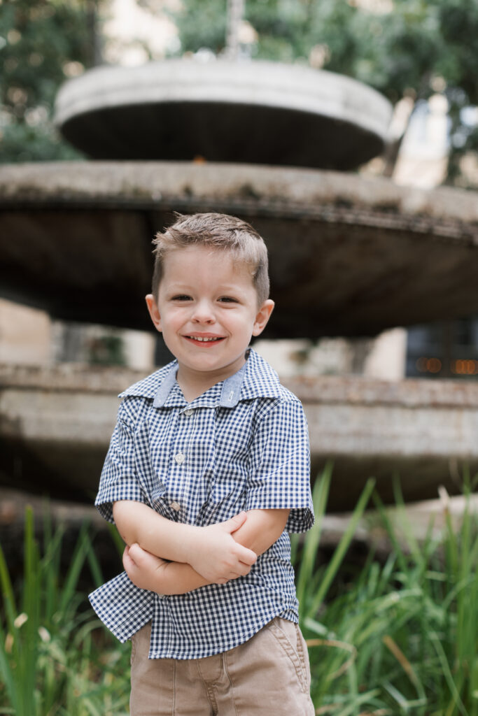 boy folds arms, standing in front of fountain