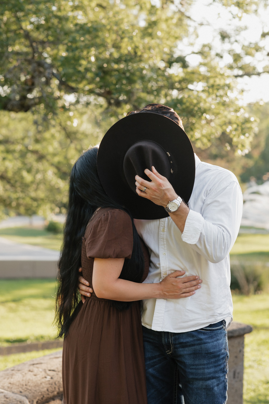 Husband and Wife kiss behind cowboy hat 