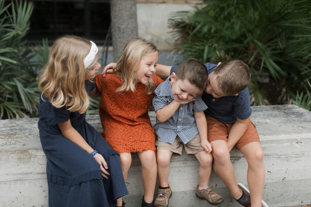 During these Family Photos at the Pearl, 4 kids laugh and giggle sitting on a bench