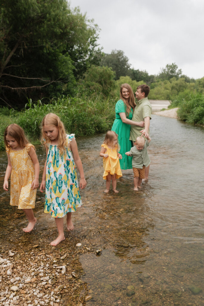 Parent's embrace looking on at their four young children. The oldest two daughters walk a short ways in front, the younger sister and brother pull on dad's arm to hurry forward