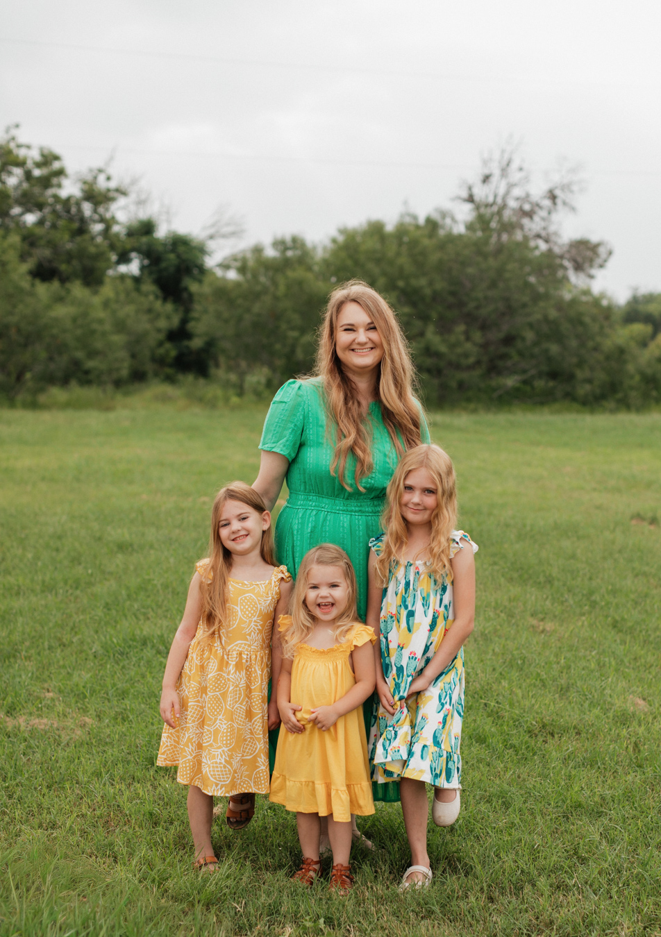 Mother and daughters, dressed in pastel summer dresses, smiling in the middle of a meadow at Crescent Bend Nature Park.